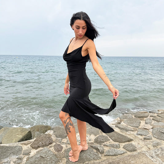 This black vintage 2000s dress features a plunging cowl neckline, and an asymmetrical ruffle hem that flutters with movement. Designed in a flattering cocktail length with a body-hugging silhouette, it’s perfect for summer nights, beach parties, or alt club looks. French-made for a dramatic, femme-fatale feel. An iconic Y2K editorial piece for minimalist seduction. Made from a polyester stretch blend. Great vintage condition.