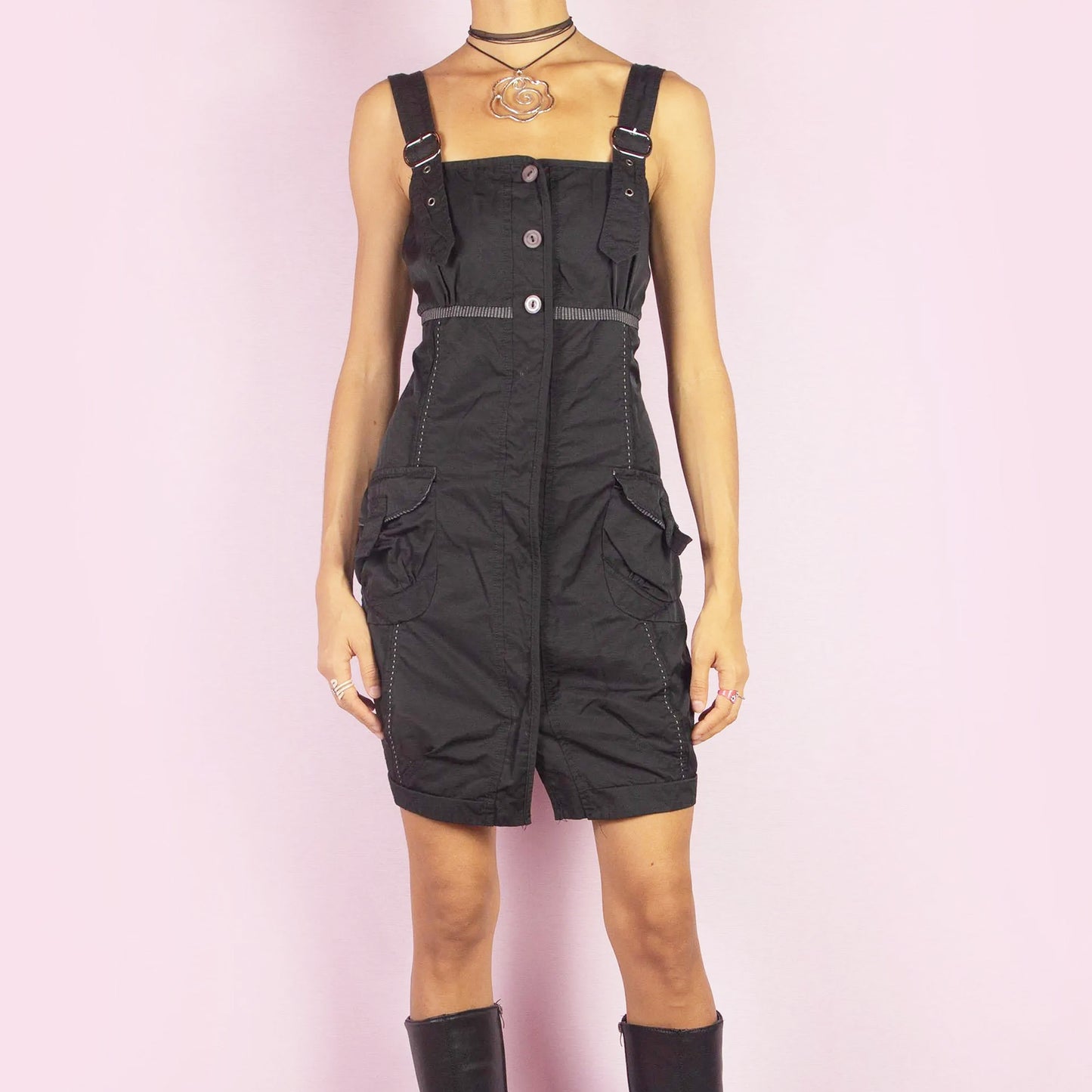 The Y2K Buckle Strap Black Mini Dress is a vintage 2000s piece featuring adjustable buckle straps, a button-down front, and utility-style pockets. Designed with contrast stitching and a structured silhouette, this mini dress is perfect for daytime looks or nights out.