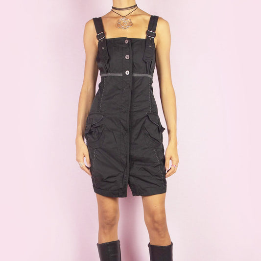 The Y2K Buckle Strap Black Mini Dress is a vintage 2000s piece featuring adjustable buckle straps, a button-down front, and utility-style pockets. Designed with contrast stitching and a structured silhouette, this mini dress is perfect for daytime looks or nights out.