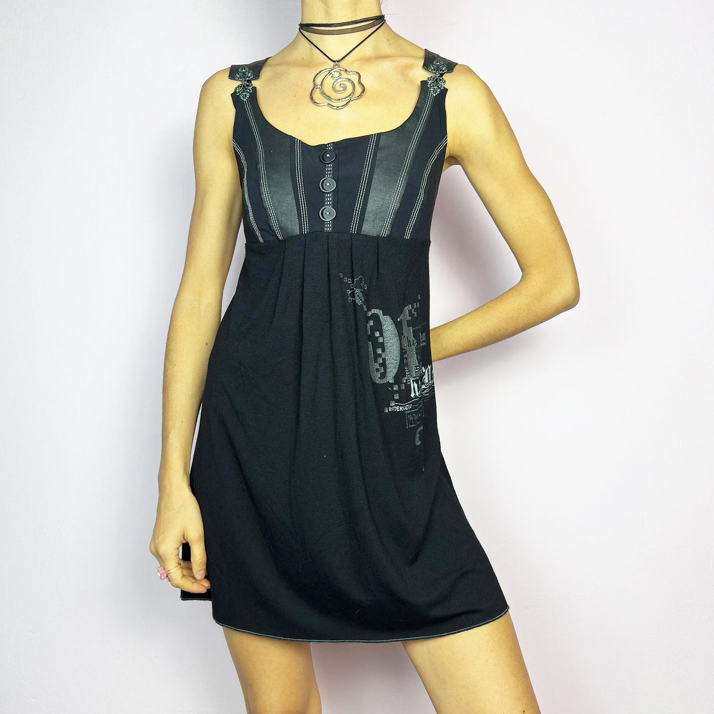 The Y2K Black Buckle Strap Mini Dress is a vintage 2000s sleeveless piece with a mix of edgy and casual aesthetics. It features decorative button details, contrast stitching, and graphic prints. The standout buckle strap details add an industrial and cyber vibe. Made from a stretchy fabric, it offers a comfortable fit, perfect for casual streetwear or alternative fashion looks. Great vintage condition.