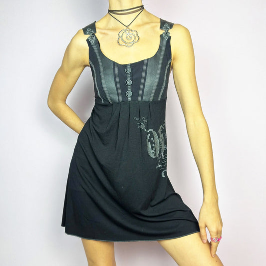 The Y2K Black Buckle Strap Mini Dress is a vintage 2000s sleeveless piece with a mix of edgy and casual aesthetics. It features decorative button details, contrast stitching, and graphic prints. The standout buckle strap details add an industrial and cyber vibe. Made from a stretchy fabric, it offers a comfortable fit, perfect for casual streetwear or alternative fashion looks.