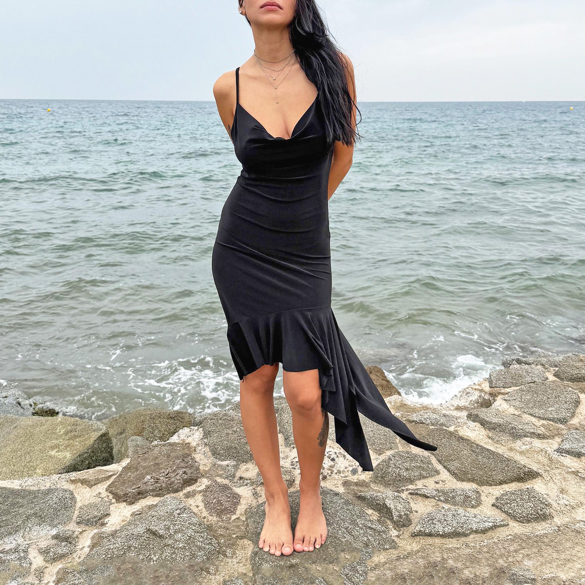 Vintage 2000s black mini dress with a plunging cowl neckline, body-hugging fit, and asymmetrical ruffle hem. Perfect for summer nights, beach parties, or club looks. Made by a French brand from a polyester stretch blend. Great vintage condition.