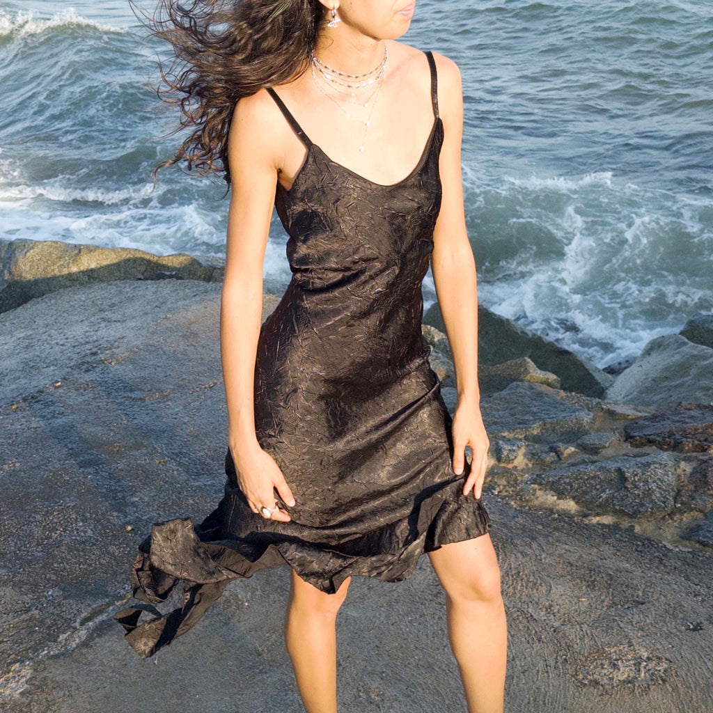 The vintage 2000s black slip dress is a made-in-France piece with crinkled texture and asymmetric ruffle hem. Its sculptural midi silhouette moves with quiet sensuality—ideal for gallery openings, formal nights, or late summer dates. A deconstructed Y2K shape that evokes avant-garde elegance, made to be seen without shouting. An archival dress crafted from a soft polyester blend. Excellent vintage condition.