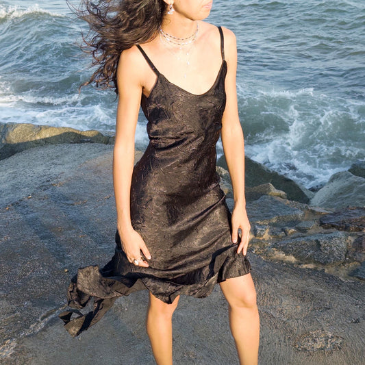 The vintage 2000s black slip dress is a made-in-France piece with crinkled texture and asymmetric ruffle hem. Its sculptural midi silhouette moves with quiet sensuality—ideal for gallery openings, formal nights, or late summer dates. A deconstructed Y2K shape that evokes avant-garde elegance, made to be seen without shouting. An archival dress crafted from a soft polyester blend. Excellent vintage condition.