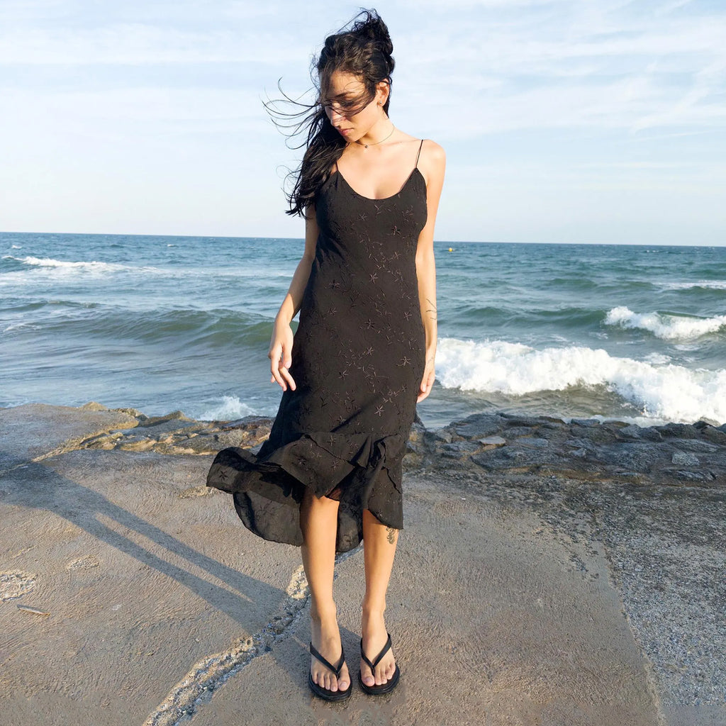 Vintage 2000s black midi dress with a slip silhouette, spaghetti straps, subtle floral embroidery, and a tiered ruffle hem that drapes asymmetrically. Lightweight and ideal for summer promenades, cocktail sunsets, or barefoot evenings. Made by a French brand. Excellent vintage condition.