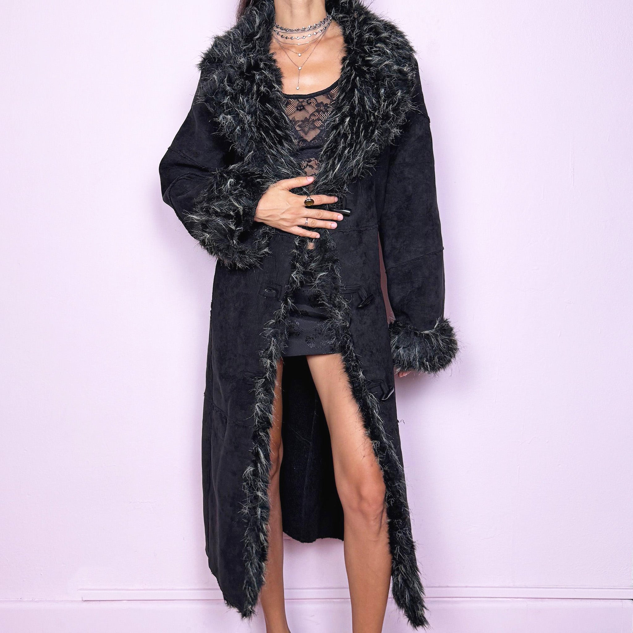 This vintage 2000s black maxi Penny Lane coat features a plush faux suede shell with dramatic black-and-beige faux fur trim at the collar and cuffs. Designed with toggle closures and side pockets, it offers warmth and structure while exuding bohemian gothic elegance. The long silhouette and textured fur detailing create a striking statement, perfect for winter nights, city wear, or whimsical Y2K layering. Made from polyester acrylic blend. Excellent vintage condition.