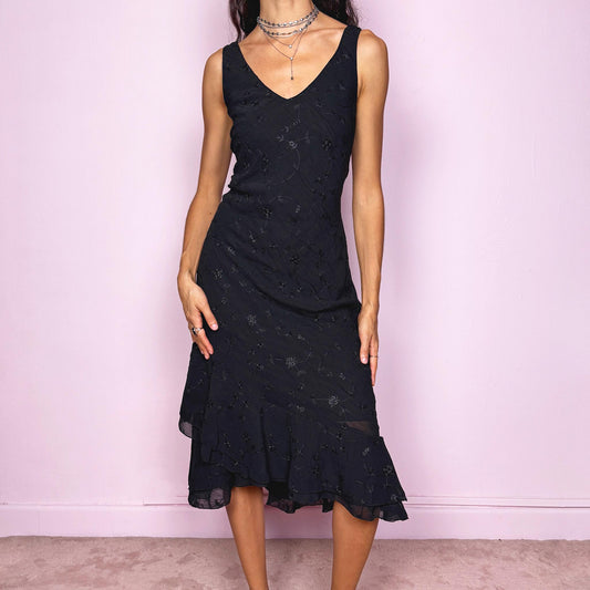 Romantic vintage 2000s black midi dress featuring delicate floral embroidery, a sleeveless cut, a V-neckline and an asymmetrical layered ruffle hem. The slightly stretchy fabric offers a comfortable, flattering fit with a minimal yet elegant look, perfect for a summer night event. Made in Spain from polyester. Excellent vintage condition.