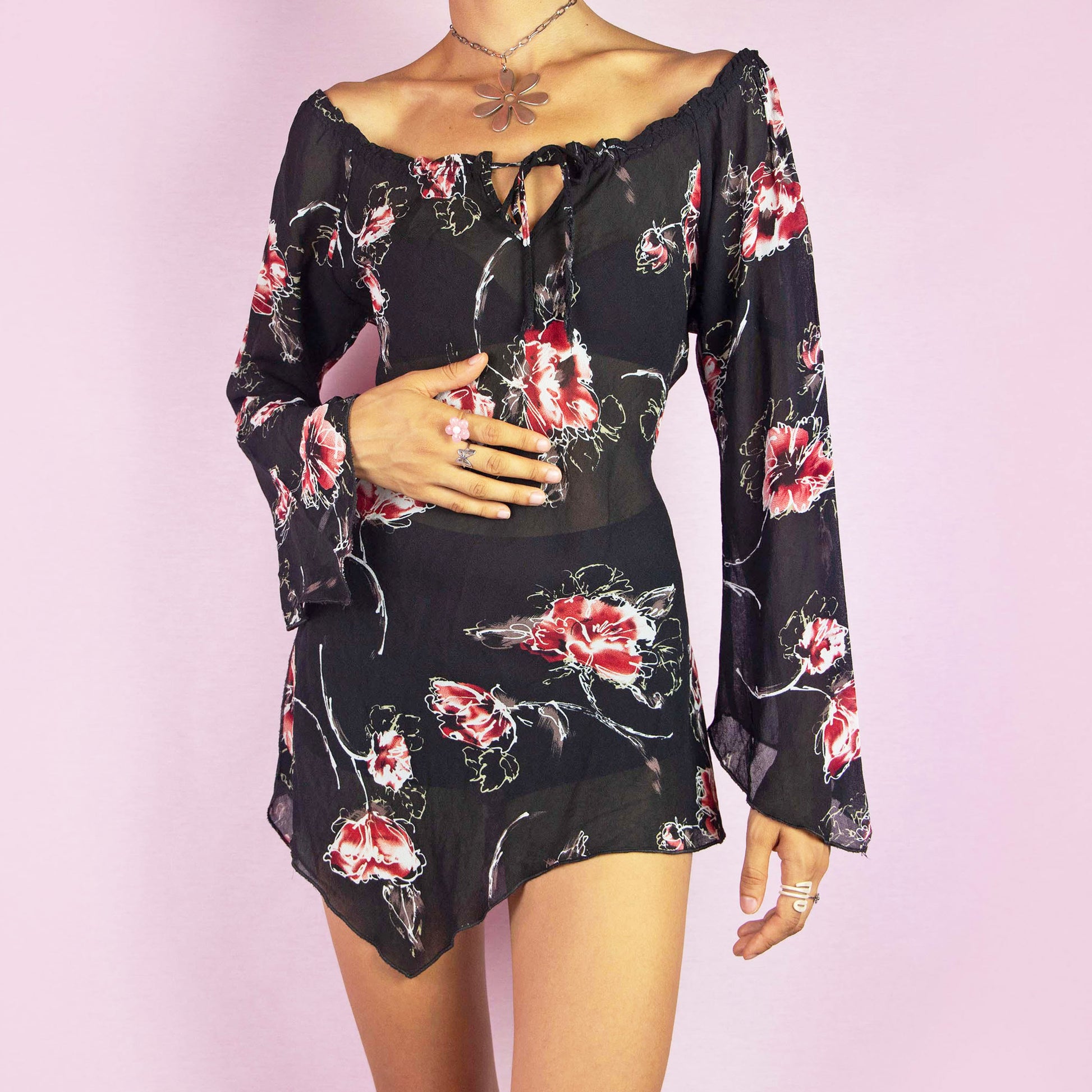 The Y2K Floral Off-Shoulder Blouse is a vintage 2000s top featuring a sheer fabric with a floral print. This blouse has an off-the-shoulder neckline with a tie detail, flared sleeves, and side slits at the hem. Its asymmetric hemline adds a romantic and bohemian vibe. Perfect for casual wear or summer events. Great vintage condition.