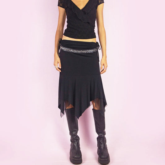 The Y2K Black Layered Asymmetric Skirt is a vintage 2000s piece featuring an avant-garde design. It has intricate bead detailing on the waist and adjustable ruched side ties. The skirt includes mesh sheer layers and a handkerchief-style asymmetric hemline, making it perfect for a bold night out look. Can be worn low rise for size XS or S. Excellent vintage condition.