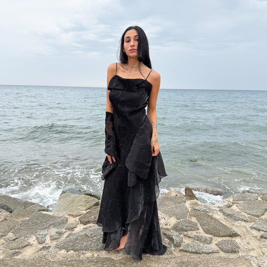 This vintage 2000s black organza-style layered slip midi dress is a French-made evening piece featuring a swirl pattern, folded neckline detail, delicate spaghetti straps, side zipper, and a flowing asymmetrical hem. It comes with a matching scarf, making it ideal for galas, proms, or dark, romantic nights. Crafted from a semi-sheer, non-stretch polyester blend. Excellent vintage condition.