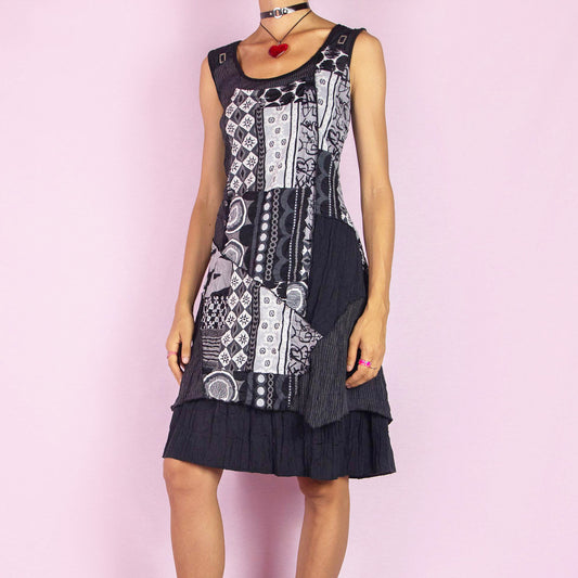 The Y2K Black Mesh Sleeveless Dress is a vintage 2000s piece featuring an abstract patchwork design with various patterns in contrasting shades of black and white. Made from stretchy fabric with printed mesh details, this mini dress offers a unique, asymmetrical hemline, perfect for casual summer wear or layered looks.