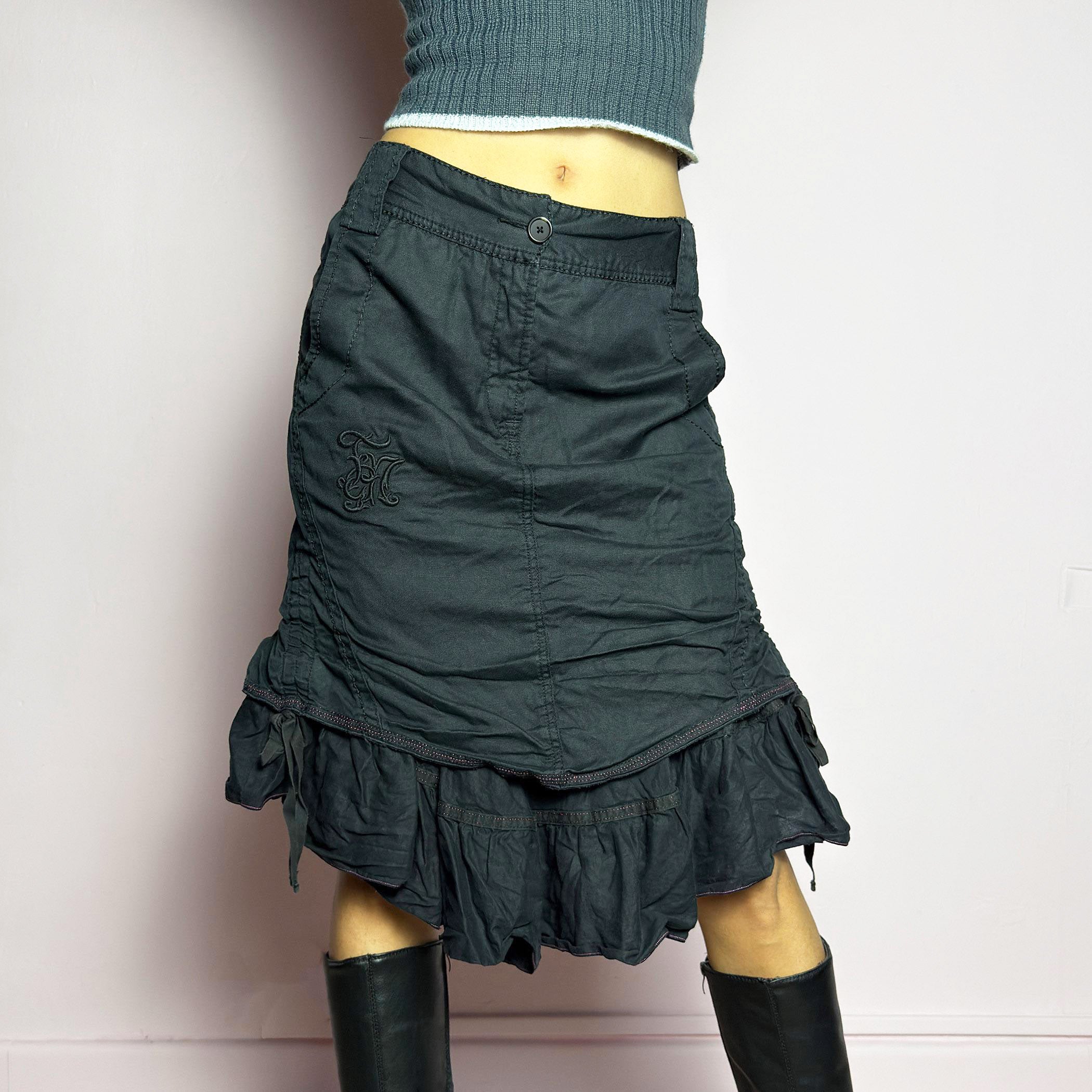 The Y2K Black Layered Skirt by Marithé François Girbaud is a vintage 2000s statement piece featuring a structured design with ruched details and ruffled layers for added texture and movement. Designed with a mid-rise fit, button and zipper closure, embroidered side detail, and an asymmetrical hem, this skirt blends edgy streetwear vibes with a playful, gothic aesthetic. Perfect for casual grunge and alternative looks.
