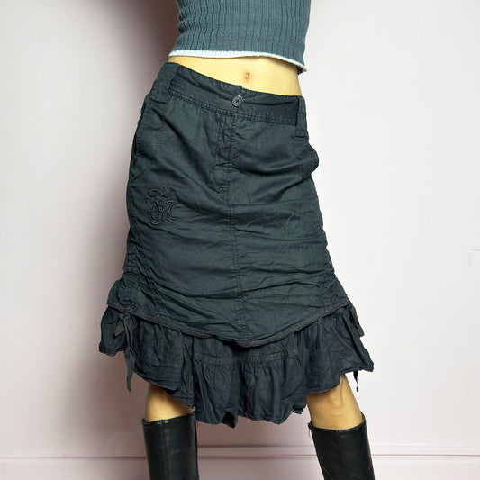 The Y2K Black Layered Skirt by Marithé François Girbaud is a vintage 2000s statement piece featuring a structured design with ruched details and ruffled layers for added texture and movement. Designed with a mid-rise fit, button and zipper closure, embroidered side detail, and an asymmetrical hem, this skirt blends edgy streetwear vibes with a playful, gothic aesthetic. Perfect for casual grunge and alternative looks.