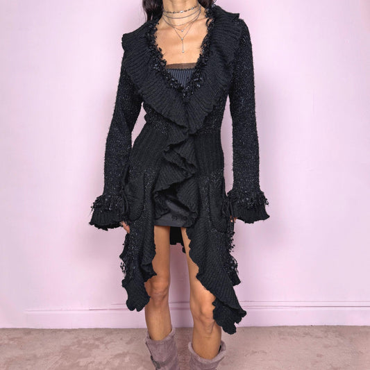 Witchy vintage 2000s black longline cardigan with dramatic ruffle neckline and dark romantic rococo style. Features bell sleeves with ruffle cuffs, two-button front closure, pockets, and asymmetric pointy hem. Whimsical fairycore silhouette, stretchy fabric for cozy winter layering. Made from polyester acrylic blend. Great vintage condition.
