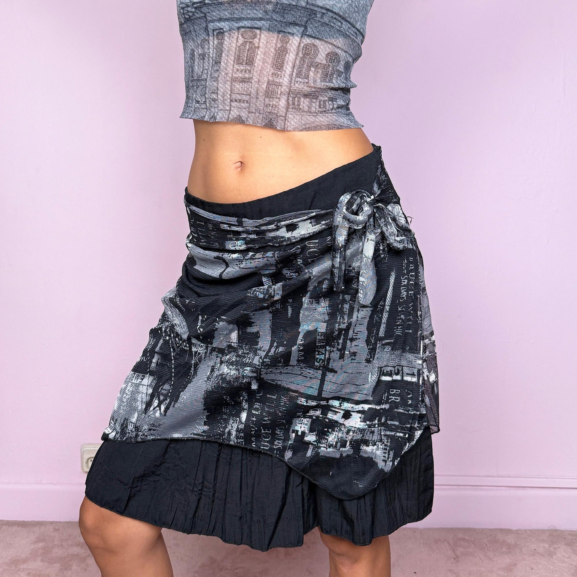 This vintage 2000s black mini skirt features a ruffle hem, side zipper closure, and semi-sheer abstract graphic mesh overlay with a tie-front detail. Its deconstructed, cyber-futuristic silhouette captures the weird girl aesthetic—perfect for night parties or streetwear looks. Can be worn low-rise in L or high-rise in XL for versatile styling. Made from a polyester blend fabric. Great vintage condition.