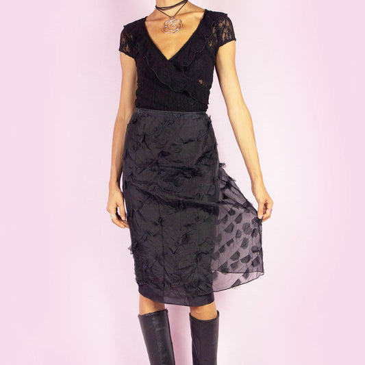The Y2K Black Applique Midi Skirt is a vintage 2000s piece featuring intricate appliqué details throughout. This elegant skirt has a side zipper closure and a flattering high-waisted fit. It is semi-sheer, making it perfect for special occasions.