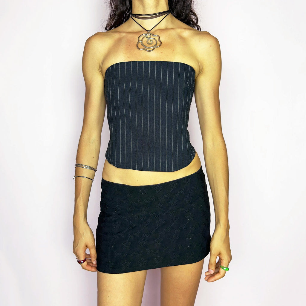 Vintage 2000s pinstripe corset top featuring a strapless silhouette with boning structure and a back zip closure for a sharp, tailored fit. Crafted in black with white stripes, it blends soft tailoring with city girl allure. Elegant yet subversive, it's ideal for cocktail hours, office party nights, or elevated downtown styling. Excellent vintage condition.