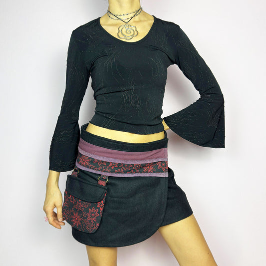 The Y2K Black Wrap Mini Skirt is a vintage 2000s piece featuring a unique wrap design with an adjustable Velcro waist for a customizable fit. Made from a thick fabric, the skirt has a contrasting waistband with floral details and a detachable utility pocket. Perfect for casual and festival looks.