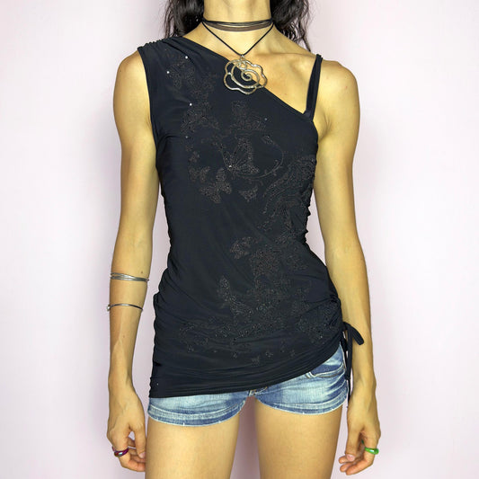 The Y2K Black Sequin Butterfly Top is a vintage 2000s asymmetrical design featuring glittery butterfly motifs, ruched sides, and dual drawstring ties at the shoulder and hem. Crafted from stretchy black fabric with a body-skimming fit, it blends glam detail with subversive edge. Ideal for party nights, clubbing, or iconic festival looks. A millennium-era classic with bold, sculptural energy. Great vintage condition.