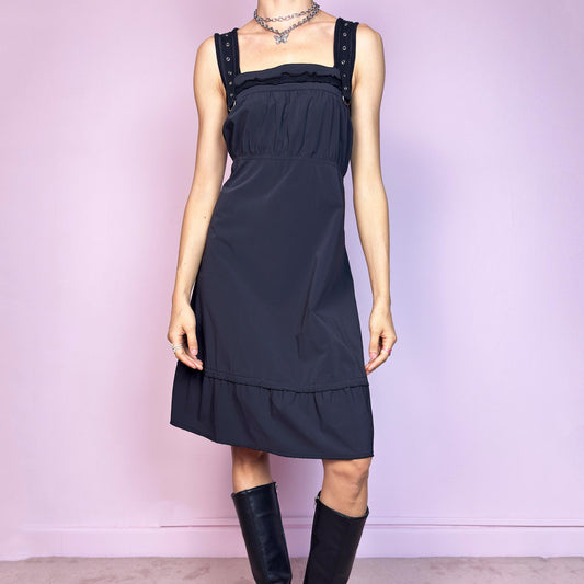 This vintage 2000s black sleeveless dress features a gathered bust, square neckline, wide grommet straps with silver hardware and a back zipper closure. The structured fabric has slight stretch, while the A-line silhouette falls to midi length with a subtle ruffle hem. A utilitarian-meets-feminine Y2K piece—minimalist and wearable with a cyber futuristic edge. Perfect for everyday summer styling with impact.