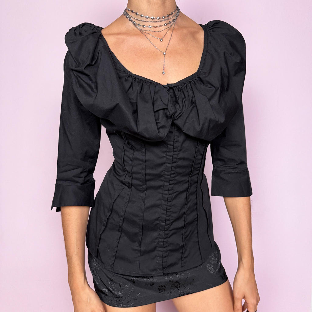 This dark avant garde vintage 2000s black blouse features a dramatic voluminous collared ruffle, a fitted pleated bodice, and three-quarter sleeves. Designed with a minimalist statement approach, it includes subtle mini hook closures and a slightly stretchy cotton–polyamide blend for a structured yet comfortable fit. The sculpted silhouette makes it ideal for formal evening looks, elegant night parties, or polished day-to-office styling. Excellent vintage condition.