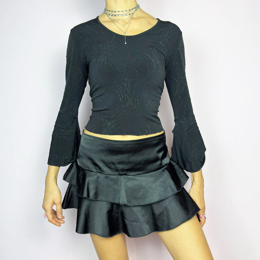 The Y2K Black Ruffle Satin Mini Skirt is a vintage 2000s piece made from a sleek satin-style stretchy fabric featuring layered ruffles, low rise design and a side zipper closure. Ideal for a night-out outfit.