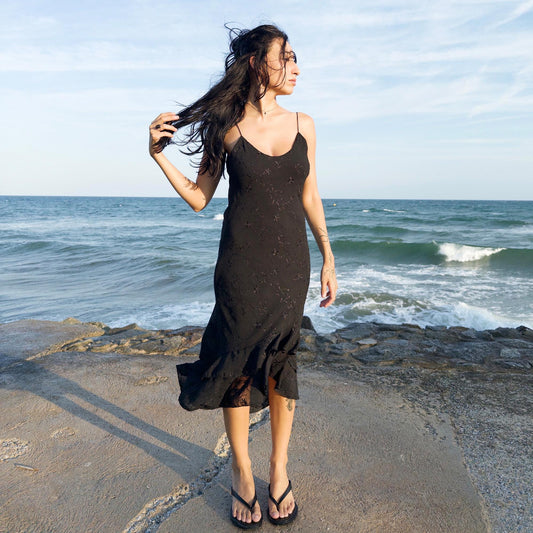 The vintage 2000s black midi dress is a French-made slip silhouette with delicate spaghetti straps and a tiered ruffle hem that drapes asymmetrically. Lightweight with subtle floral embroidery, it flows with ease—ideal for summer promenades, cocktail sunsets, or barefoot evenings. Its understated sensuality and effortless cut evoke a romantic calm. Excellent vintage condition.