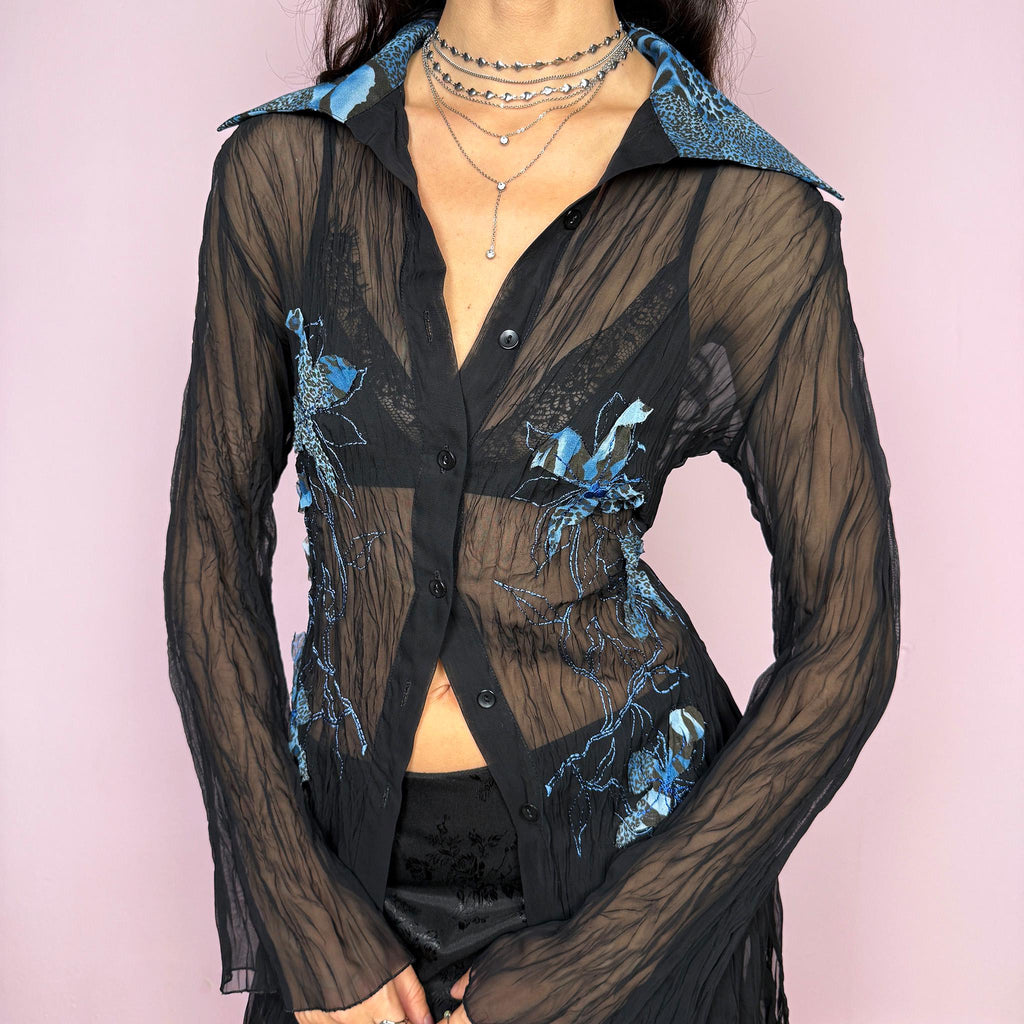 Elegant vintage 2000s black sheer longline blouse featuring blue floral embroidered appliqués with subtle leopard print, flared long sleeves, collared neckline, and side slits. Button-down front perfect for party nights or formal evening events. By French brand. Excellent vintage condition.