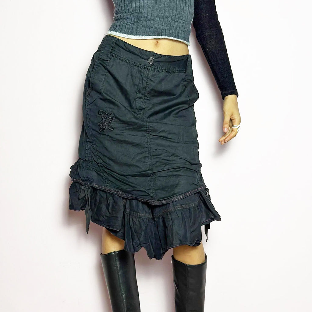 The Y2K Black Layered Skirt by Marithé François Girbaud is a vintage 2000s statement piece featuring a structured design with ruched details and ruffled layers for added texture and movement. Designed with a mid-rise fit, button and zipper closure, embroidered side detail, and an asymmetrical hem, this skirt blends edgy streetwear vibes with a playful, gothic aesthetic. Perfect for casual grunge and alternative looks.