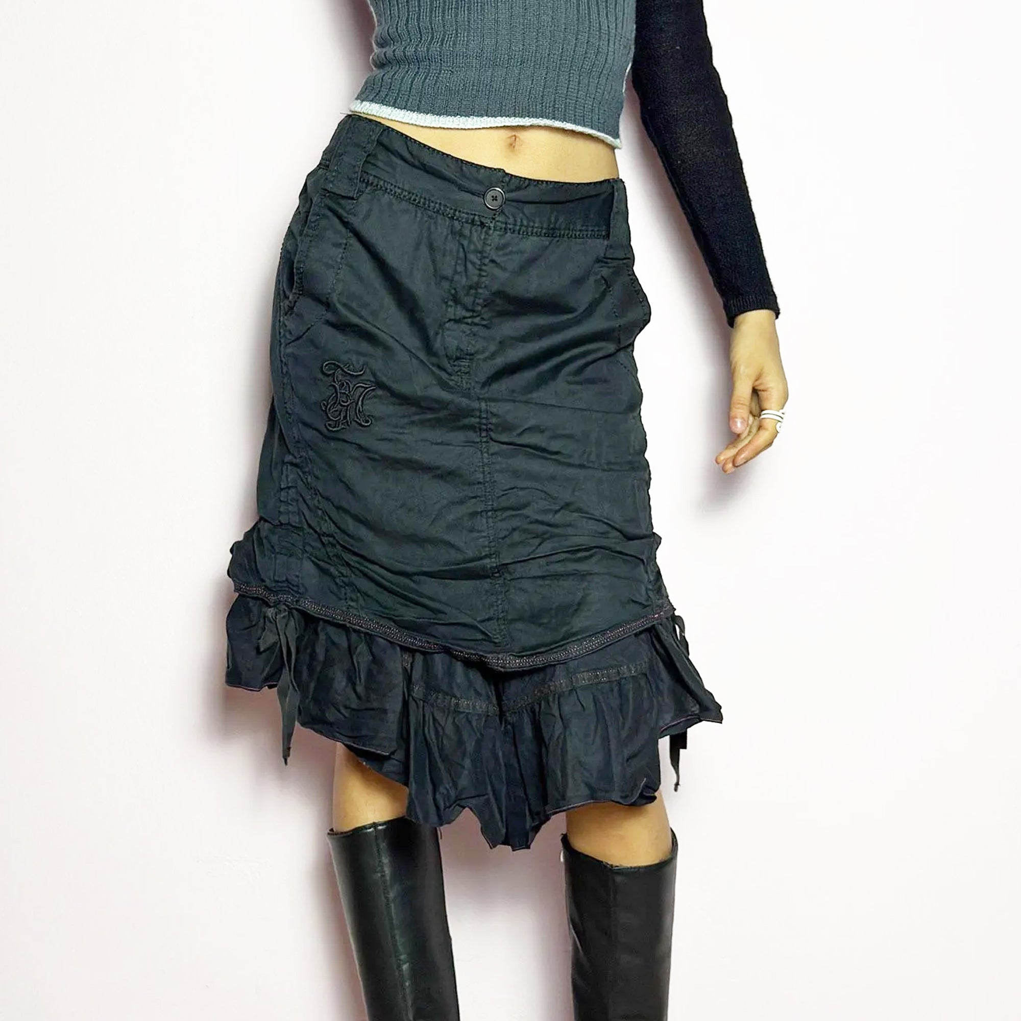 The Y2K Black Layered Skirt by Marithé François Girbaud is a vintage 2000s statement piece featuring a structured design with ruched details and ruffled layers for added texture and movement. Designed with a mid-rise fit, button and zipper closure, embroidered side detail, and an asymmetrical hem, this skirt blends edgy streetwear vibes with a playful, gothic aesthetic. Perfect for casual grunge and alternative looks.