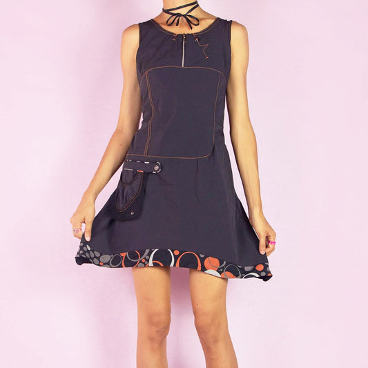 The Y2K Black Sleeveless Mini Dress is a vintage 2000s piece featuring a scoop neckline and a fitted silhouette made from stretchy fabric. This unique dress includes a zip-up front, a side pocket, and contrast stitching. It also features an asymmetric pointed hem with a geometric print trim. Perfect for parties and night events.