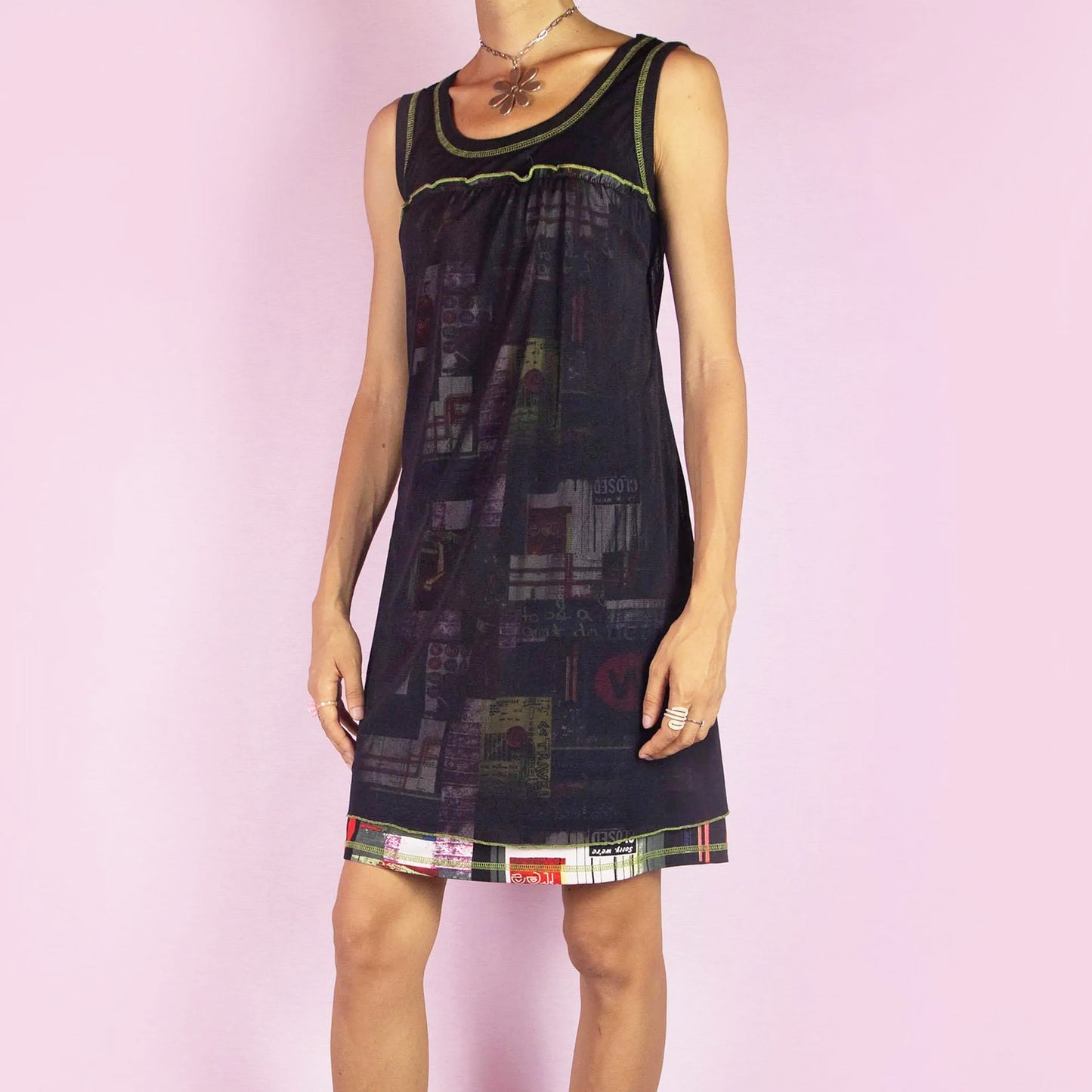 The Y2K Black Sleeveless Mesh Dress is a vintage 2000s mini dress featuring a scoop neckline, relaxed fit, and lightweight mesh fabric. The dress is adorned with abstract prints and neon green stitching along the neckline and hem. Its layered design and playful details make it perfect for casual summer outings.