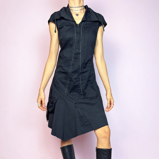 This vintage 2000s black techwear dress features cap sleeves, a dramatic asymmetric hem, and sculptural paneling for a bold silhouette. Made from a stretchy fabric, it includes a side zip closure and ruched utility pocket. Decorative topstitching and a funnel-style collar with drawstrings elevate the structure. Mid-length and lightweight, perfect for summer. A sleek statement in futuristic edge. Great vintage condition.