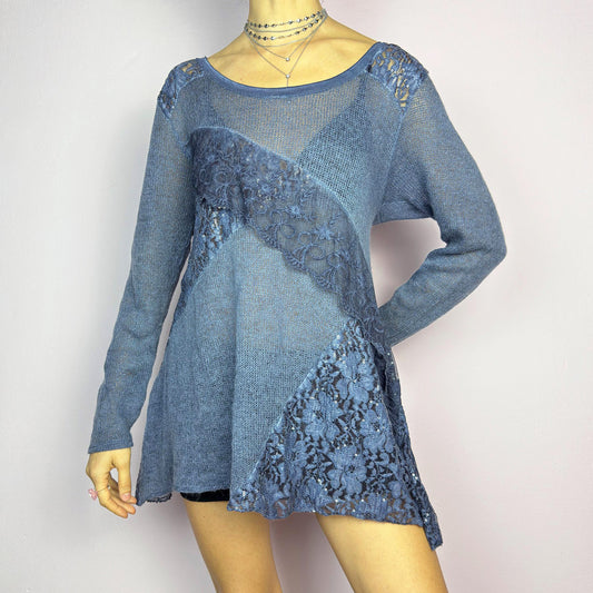 The Y2K Blue Lace Asymmetric Sweater is a vintage 2000s piece featuring a semi-sheer knit design with delicate lace and sequin paneling in an asymmetrical pattern. Designed with a scoop neckline, long sleeves, and a flowy silhouette, this sweater tunic adds a dreamy, romantic touch to any outfit. Perfect for layering in autumn and winter. Excellent vintage condition.