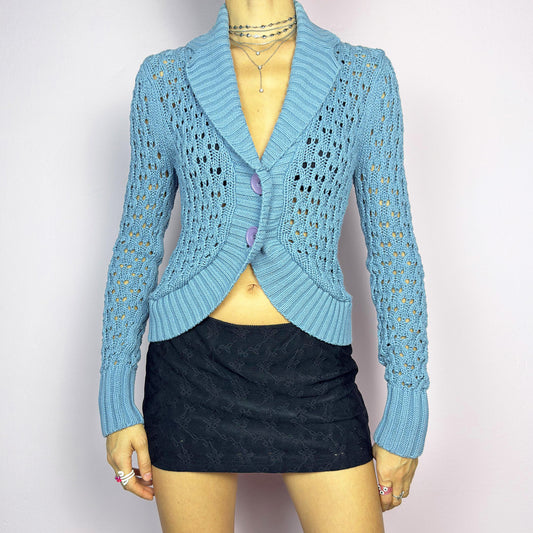 The Y2K Blue Open Knit Cardigan is a vintage 2000s charming and cozy bolero. This cropped cardigan features a textured open-knit design, a light blue tone and large buttons on the front. Perfect for layering to create a casual ensemble. Made from a cotton yarn. Excellent vintage condition.