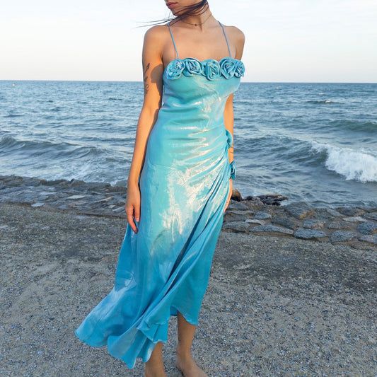 The vintage 2000s blue slip dress is a French-made fantasy with sculptural rosette appliqué along the bust and ruched side detail. Its iridescent finish and fluid midi length evoke a dreamy softness, perfect for proms, summer weddings, or romantic evenings. The silhouette is both delicate and structured, capturing quiet glamour with fairytale allure. A romantic Y2K archive crafted from a shimmering non-stretch fabric. Great vintage condition.