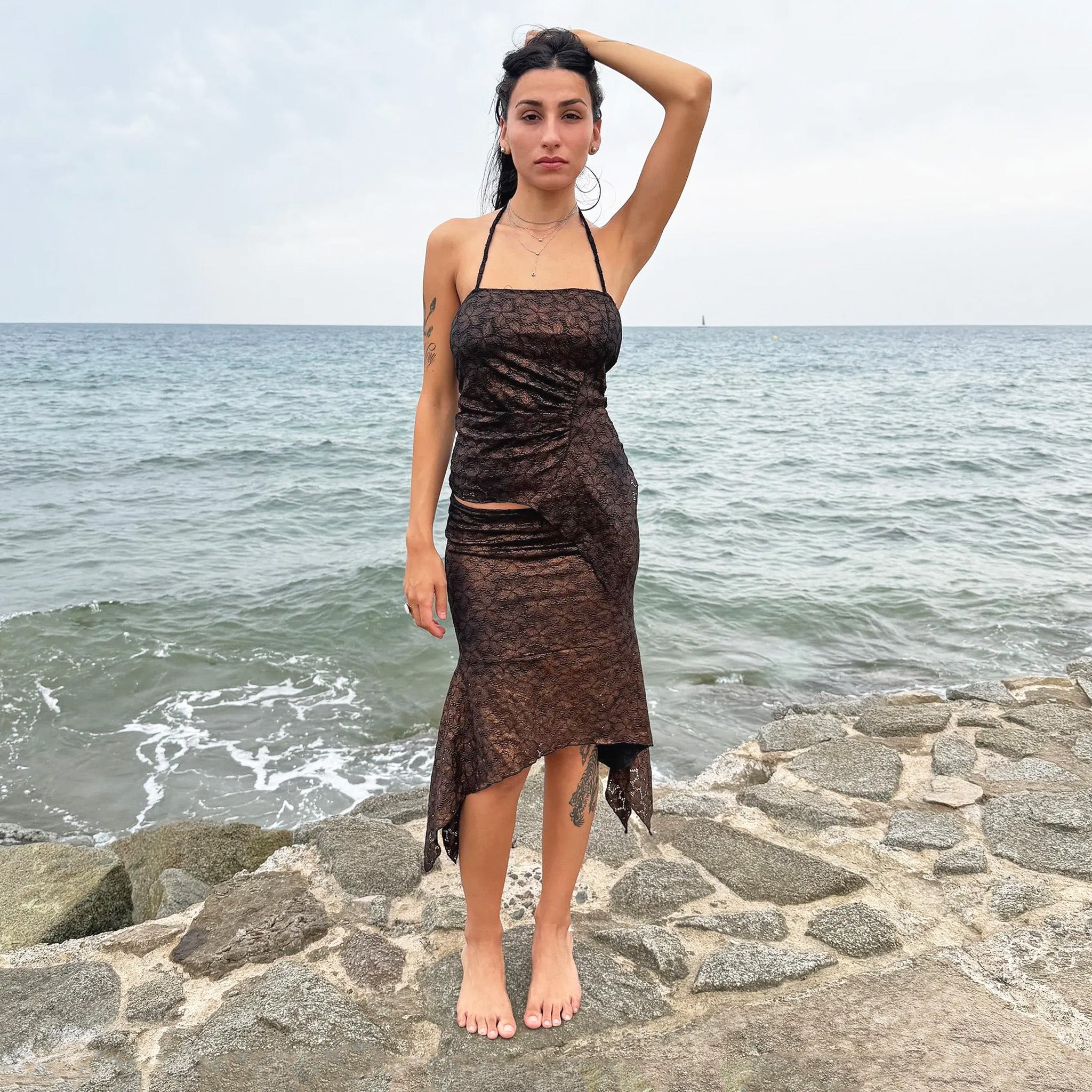 Vintage 2000s two-piece set in shiny dark bronze-copper with a black lace pattern. Features a handkerchief-style asymmetric midi skirt with elastic waist and a matching ruched halter tie-neck top with an asymmetrical pointed hem. Perfect for festivals, summer nights, or dark whimsical styling. Made in Spain from a stretchy polyester blend. Excellent vintage condition.