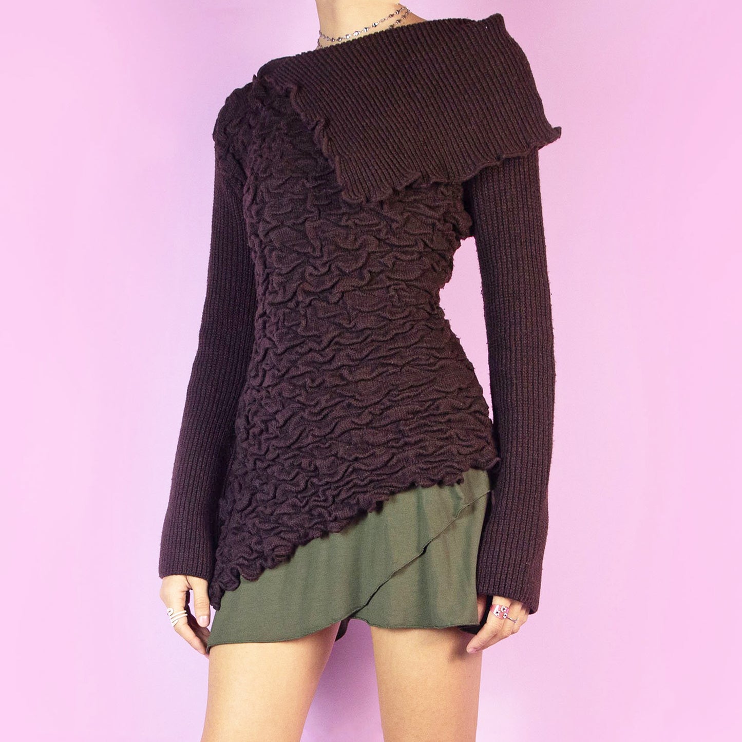 The Y2K Brown Asymmetric Knit Sweater is a vintage 2000s dark brown pullover with a distinct asymmetric design, a textured, crinkle-knit pattern across the body, complemented by a ribbed knit panel that drapes elegantly over one shoulder. Perfect for adding an avant-garde touch to your autumn or winter wardrobe. Made from a soft acrylic-polyester blend. Excellent vintage condition.