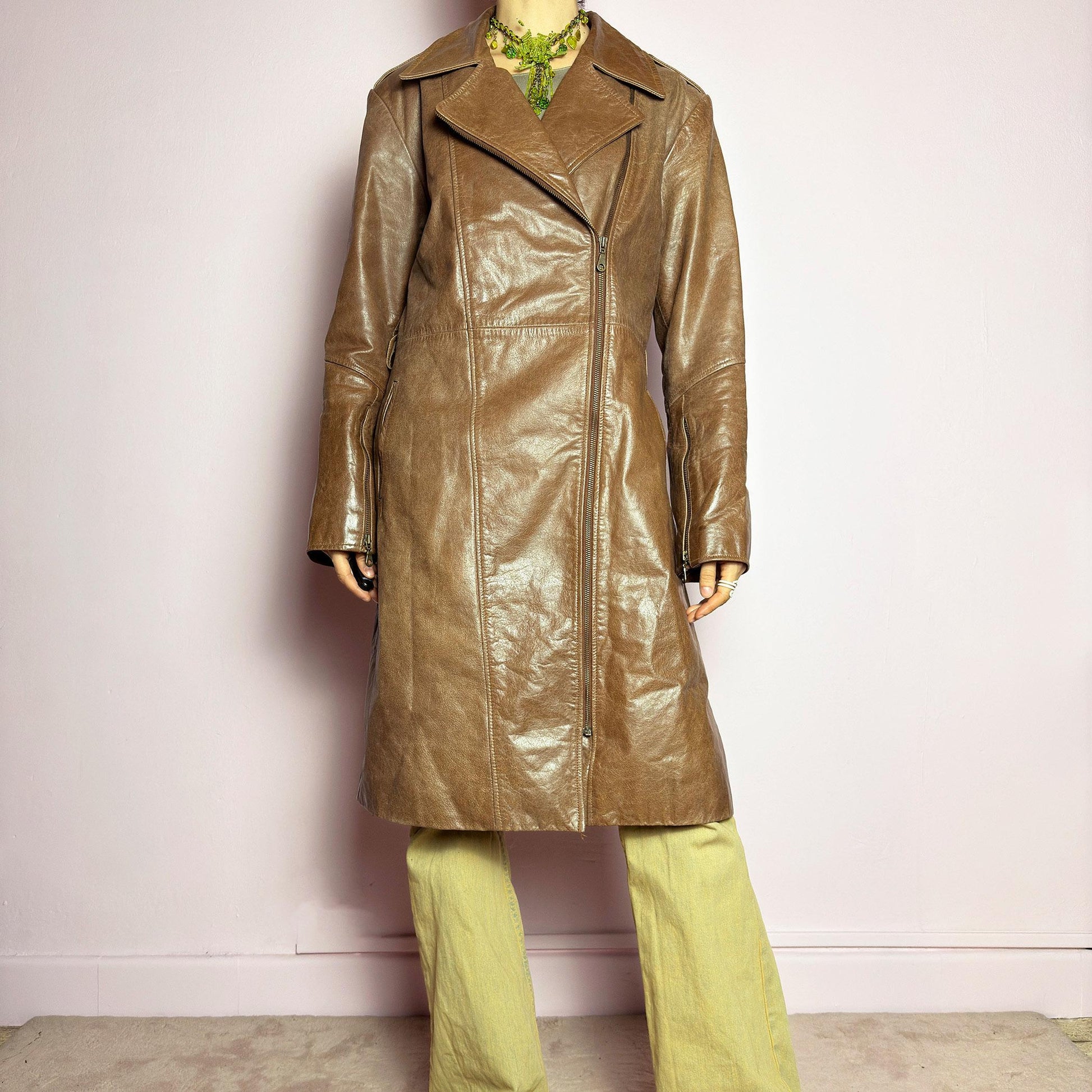The Y2K Long Brown Leather Coat is a heavy, structured vintage 2000s piece crafted from genuine leather. It features an asymmetrical zip closure, a wide lapel collar, and a belted waist for a cinched silhouette. The coat includes pockets and a smooth lining for comfort. With its durable construction and timeless design, this vintage long leather coat is perfect for edgy streetwear or sophisticated layering. adult world shop