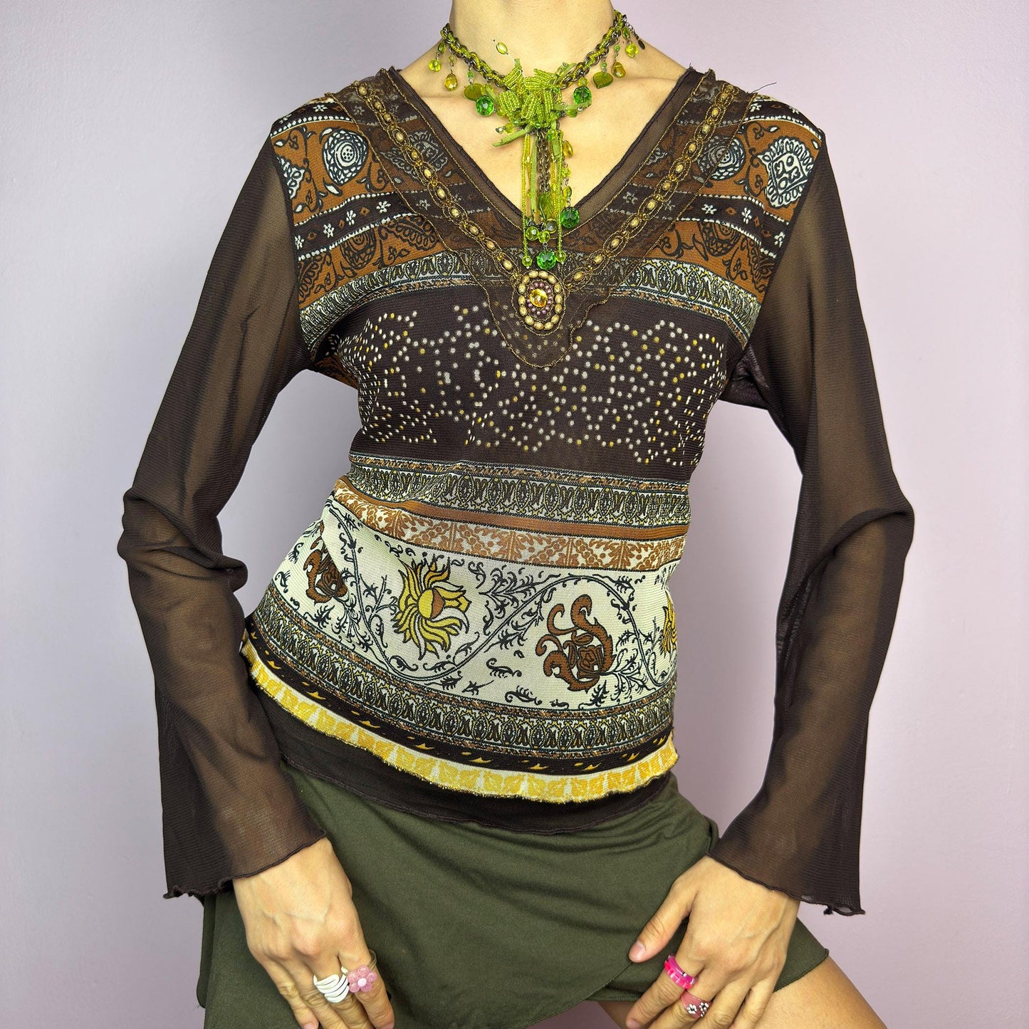 The Y2K Brown Bell Sleeve Mesh Top is a vintage 2000s piece featuring a semi-sheer mesh fabric with baroque and floral-inspired prints. Designed with flared bell sleeves, a fitted silhouette, and a layered hem, this top embodies a dreamy bohemian aesthetic. The lightweight and stretchy fabric make it perfect for ethereal, fairy-grunge looks. adult world shop