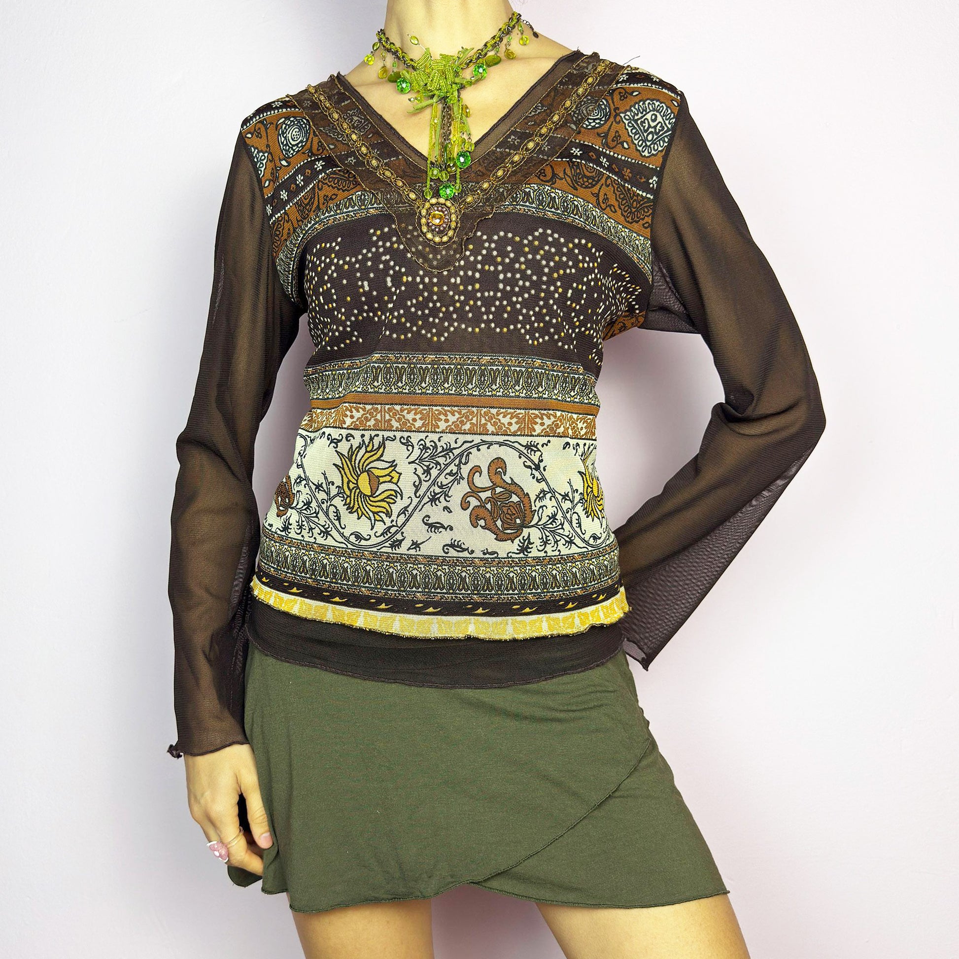 The Y2K Brown Bell Sleeve Mesh Top is a vintage 2000s piece featuring a semi-sheer mesh fabric with baroque and floral-inspired prints. Designed with flared bell sleeves, a fitted silhouette, and a layered hem, this top embodies a dreamy bohemian aesthetic. The lightweight and stretchy fabric make it perfect for ethereal, fairy-grunge looks. Excellent vintage condition.