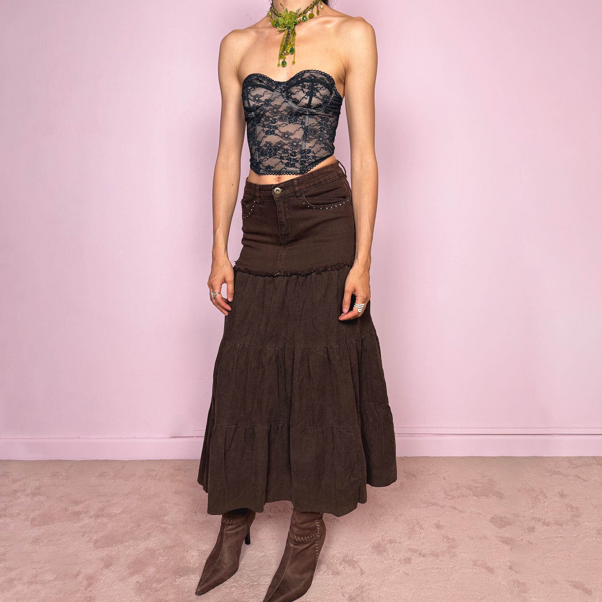 Vintage 2000s dark brown tiered corduroy maxi skirt with a bohemian/western Y2K feel, featuring a fitted denim-style upper panel, rhinestone pocket details, raw-edge trim, and a flowing gathered tiered silhouette. Made from a stretchy 65% cotton-blend fabric, the skirt has an earthy, romantic look. Can be worn high-waisted for size XS or lower-rise for XXS. Excellent vintage condition.
