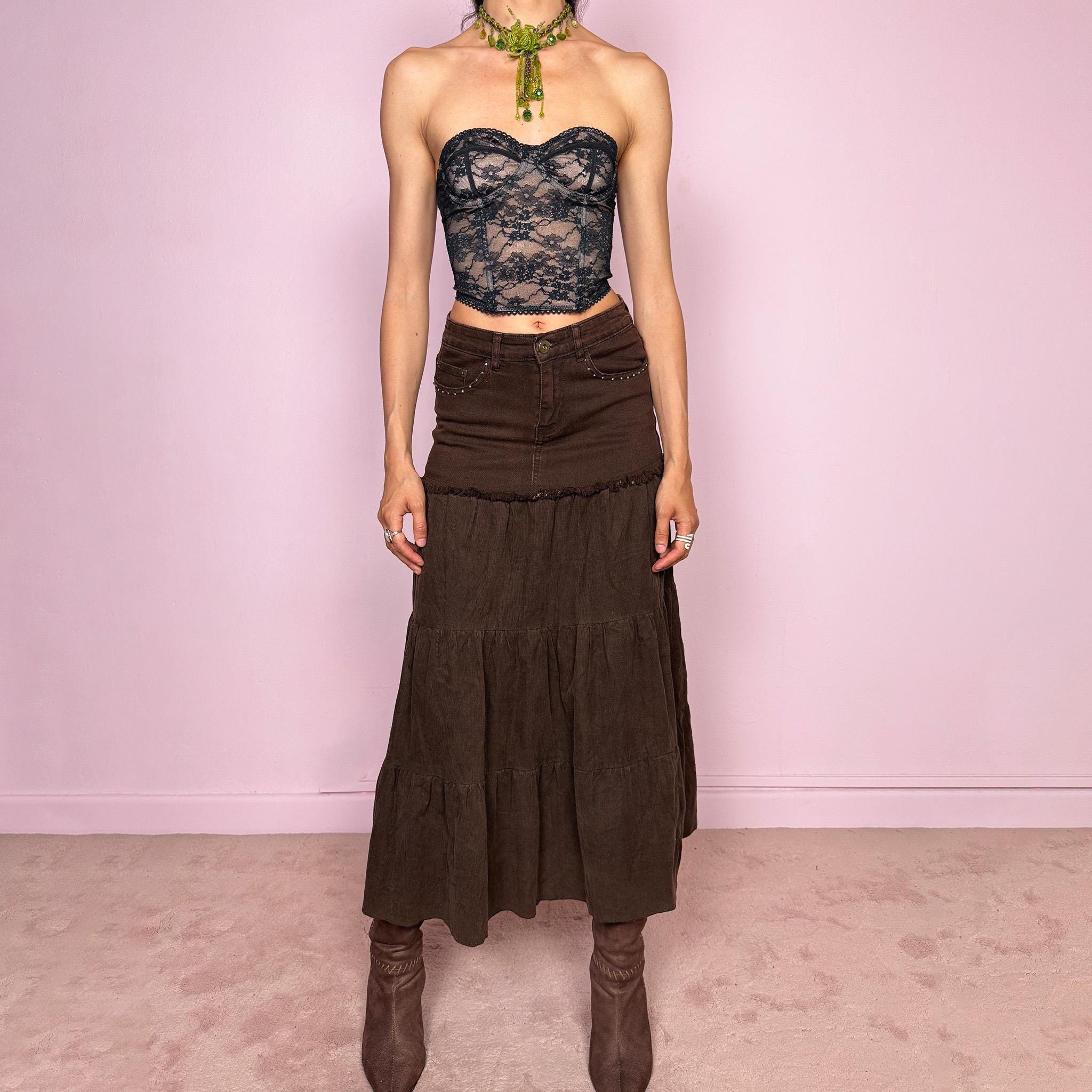 Vintage 2000s dark brown tiered corduroy maxi skirt with a bohemian/western Y2K feel, featuring a fitted denim-style upper panel, rhinestone pocket details, raw-edge trim, and a flowing gathered tiered silhouette. Made from a stretchy 65% cotton-blend fabric, the skirt has an earthy, romantic look. Can be worn high-waisted for size XS or lower-rise for XXS. Excellent vintage condition.