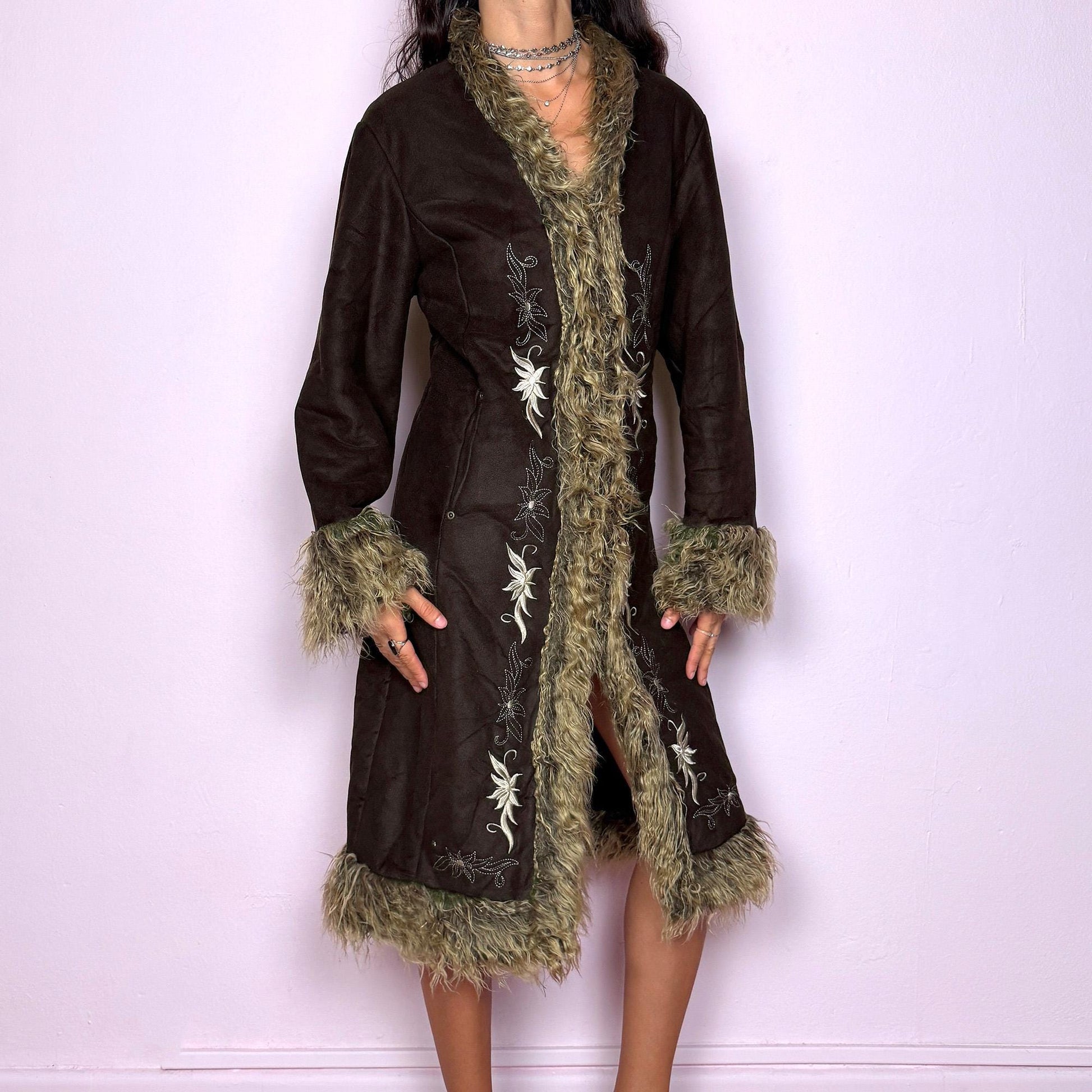 This vintage 2000s dark brown Penny Lane coat features beige faux fur trim at the collar, cuffs, and hem, with intricate floral embroidery along the front. Crafted from soft faux suede with pockets and dual snap-and-hook closure, it embodies the whimsical 70s Afghan-inspired Y2K aesthetic. Warm and romantic—perfect for fairycore, boho, and forest muse styling. Made from polyester faux suede and faux fur. Great vintage condition.