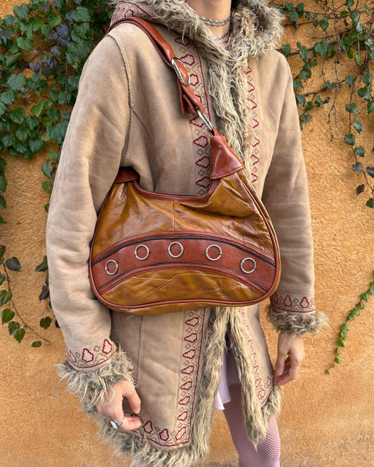 Vintage 2000s brown and mustard-brown faux leather shoulder bag with classic Y2K city-girl appeal. Features metal O-ring details across the front, contrast paneling, and a secure double zip closure. The slouchy silhouette makes it perfect as a bold 2000s statement everyday bag or a party-night accessory. Excellent vintage condition.