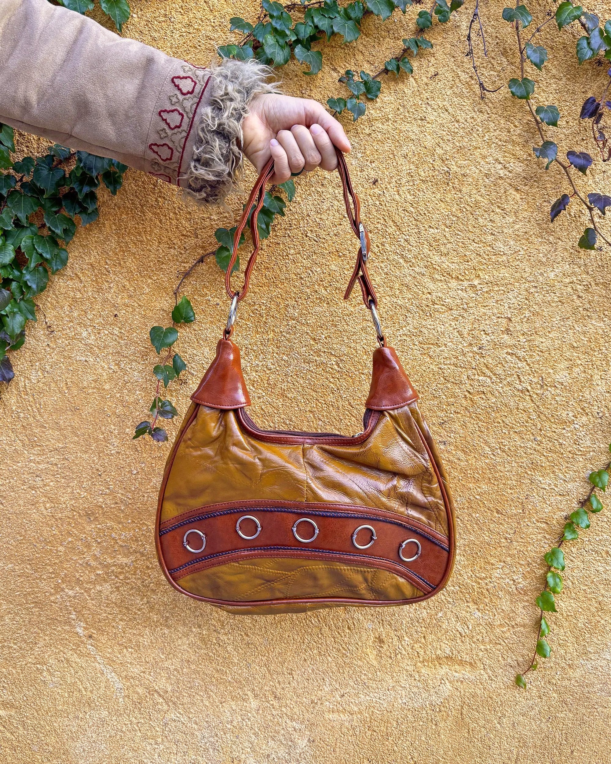 Vintage 2000s brown and mustard-brown faux leather shoulder bag with classic Y2K city-girl appeal. Features metal O-ring details across the front, contrast paneling, and a secure double zip closure. The slouchy silhouette makes it perfect as a bold 2000s statement everyday bag or a party-night accessory. Excellent vintage condition.
