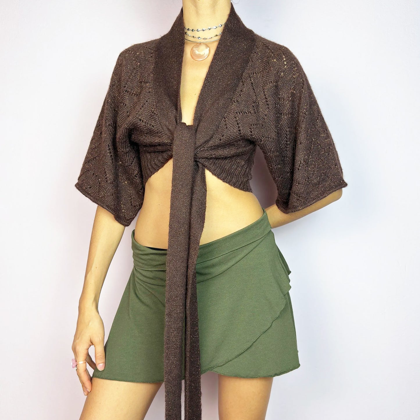 The Y2K Brown Knit Cardigan Bolero is a chic vintage 2000s piece. This cropped bolero features an open-knit design, short sleeves, and a long tie-front closure for an adjustable fit. Its warm brown tone is enhanced with a hint of metallic threading for a touch of shimmer. Perfect for layering. Great vintage condition.