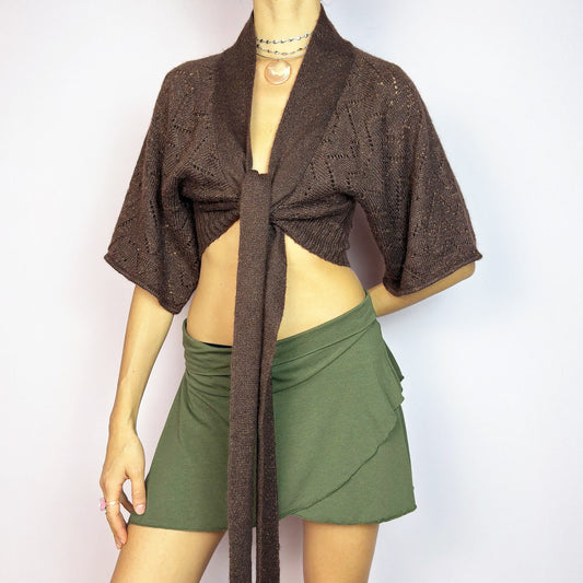 The Y2K Brown Knit Cardigan Bolero is a chic vintage 2000s piece. This cropped bolero features an open-knit design, short sleeves, and a long tie-front closure for an adjustable fit. Its warm brown tone is enhanced with a hint of metallic threading for a touch of shimmer. Perfect for layering. Great vintage condition.