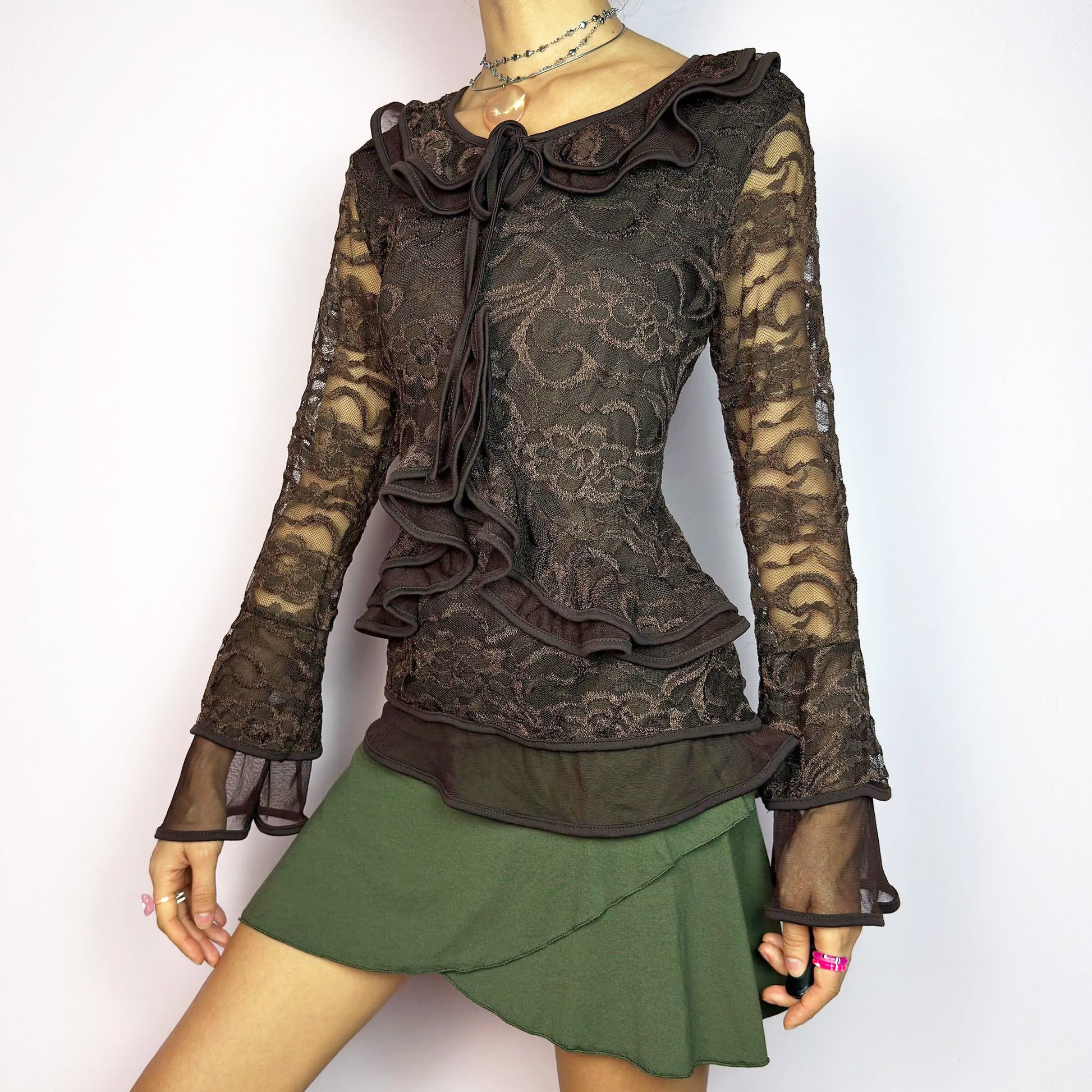 The Y2K Brown Lace Ruffle Top is a vintage 2000s statement piece, showcasing intricate floral lace throughout for a romantic and feminine look. This top features a stretchy semi-sheer fabric, layered ruffles along the neckline and front, flared mesh sleeves with bell cuffs, and a tie detail at the collar. Perfect for whimsical goth inspired outfits. Excellent vintage condition.