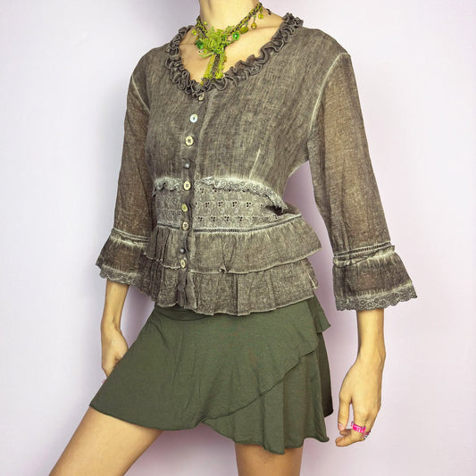This vintage 2000s brown ruffle frill blouse features a faded wash with lace trims, tiered ruffle panels, and a romantic fairy-grunge mood. The button-up front and 3/4 bell sleeves blend cottagecore and bohemian cues for dreamy summer styling or layered spring looks. Made from a cotton linen polyester blend. Excellent vintage condition.